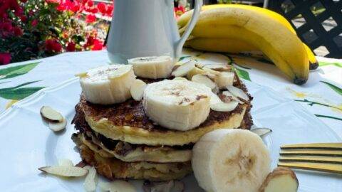 stack of almond flour pancakes with banana, almonds and syrup.