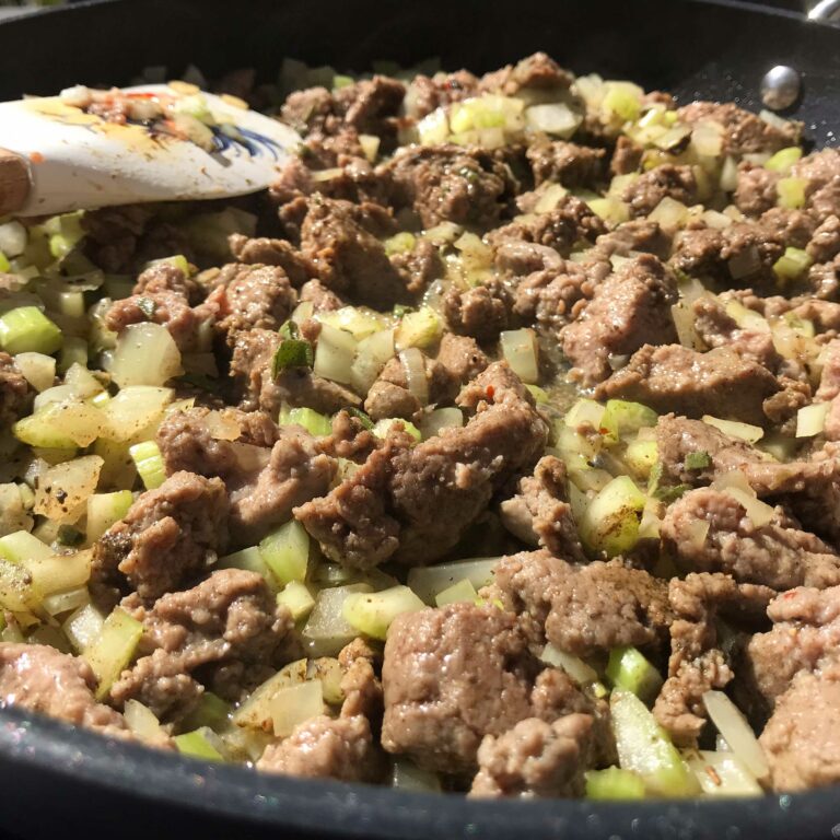 sausage cooking with veggies in skillet.