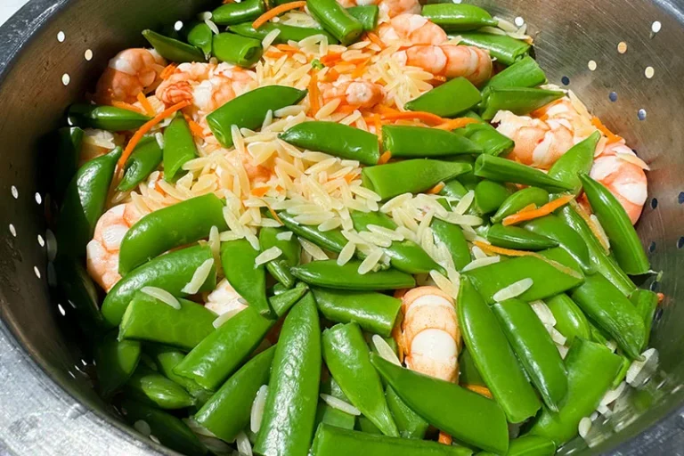 cooked shrimp, orzo, carrots and snap peas draining in colander.