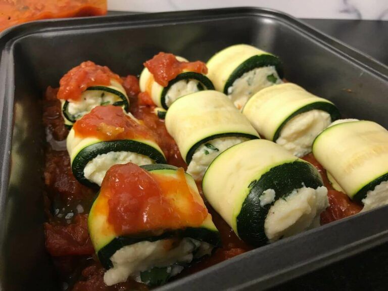 full pan of zucchini rollups with sauce on top of some of them
