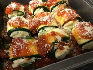 All the zucchini roll ups in a pan topped with sauce and parmesan cheese