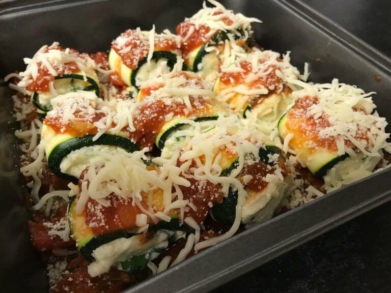 all zucchini roll ups in a pan topped with sauce, parmesan and mozzarella