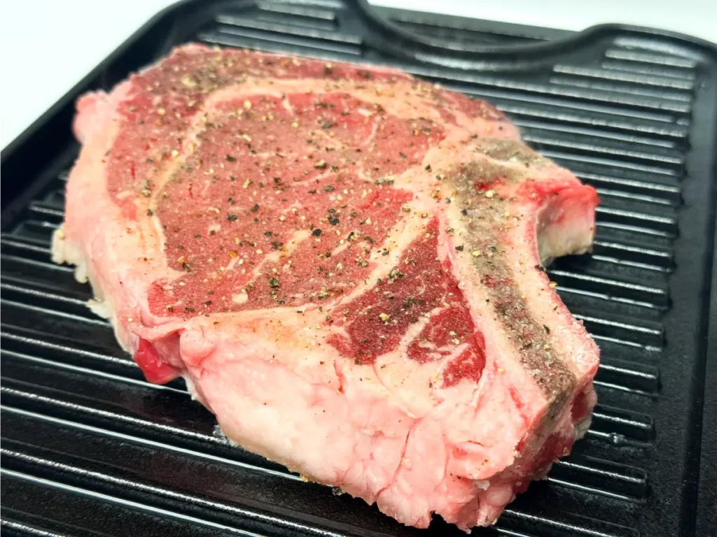 Ribeye steak resting on a hot grill pan.