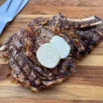 Grilled ribeye steak topped with slices of butter.