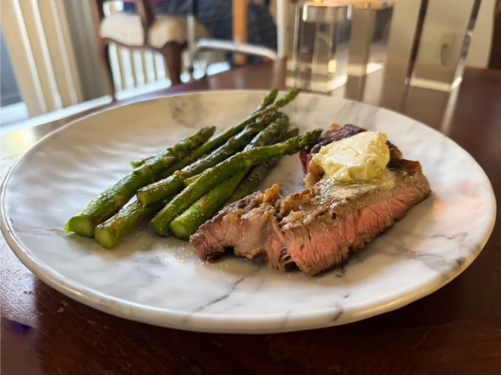 A plate of grilled asparagus and a juicy steak topped with butter.