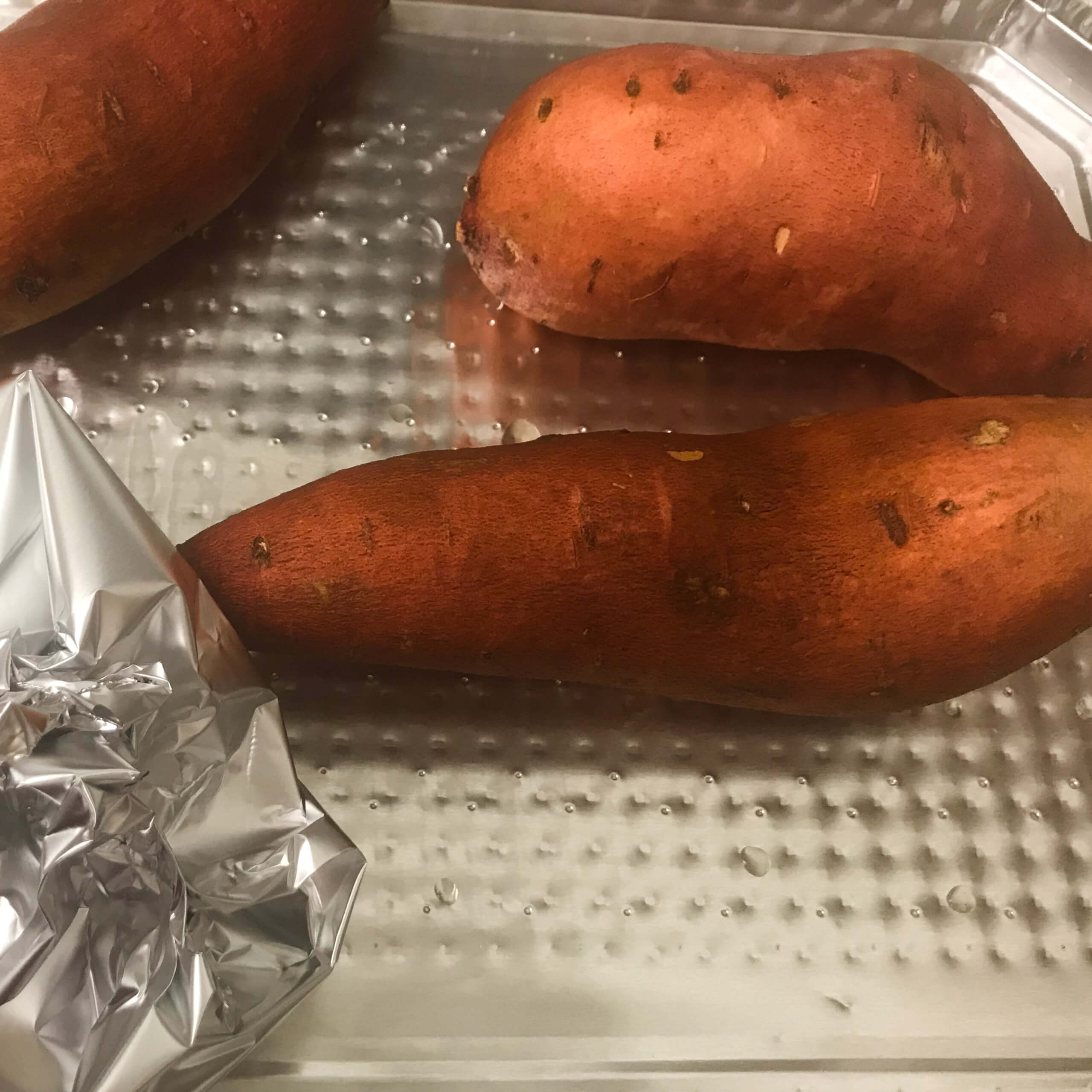 sweet potatoes and wrapped garlic on baking tray