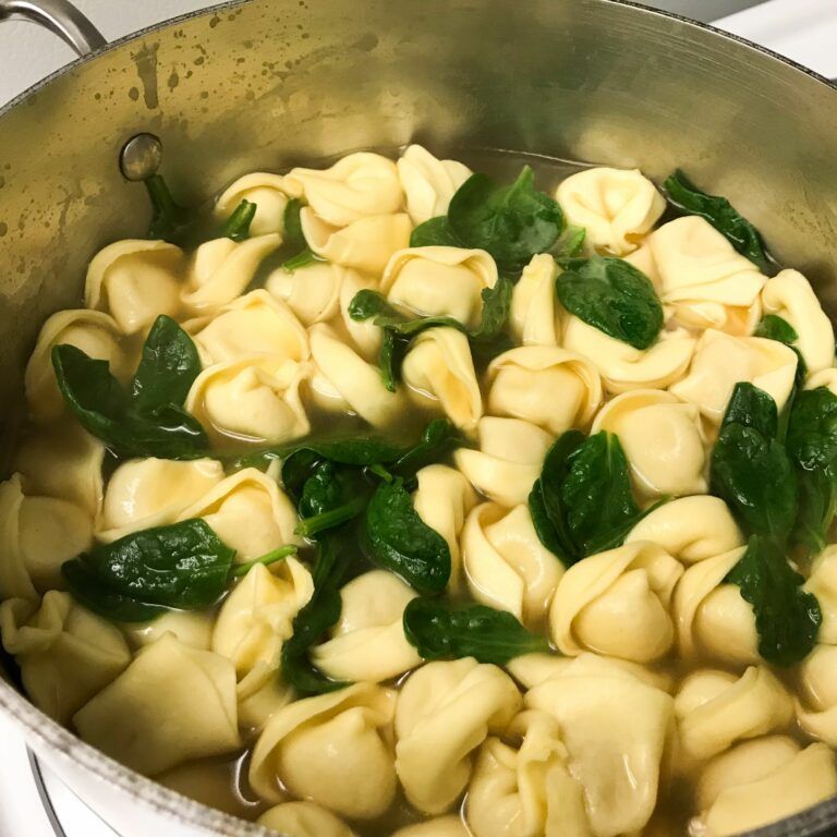 spinach and cheese tortellini cooking in broth on stove