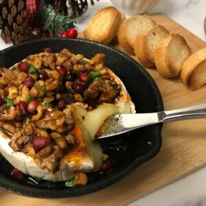 baked brie with knife on cutting board with baguette slices.