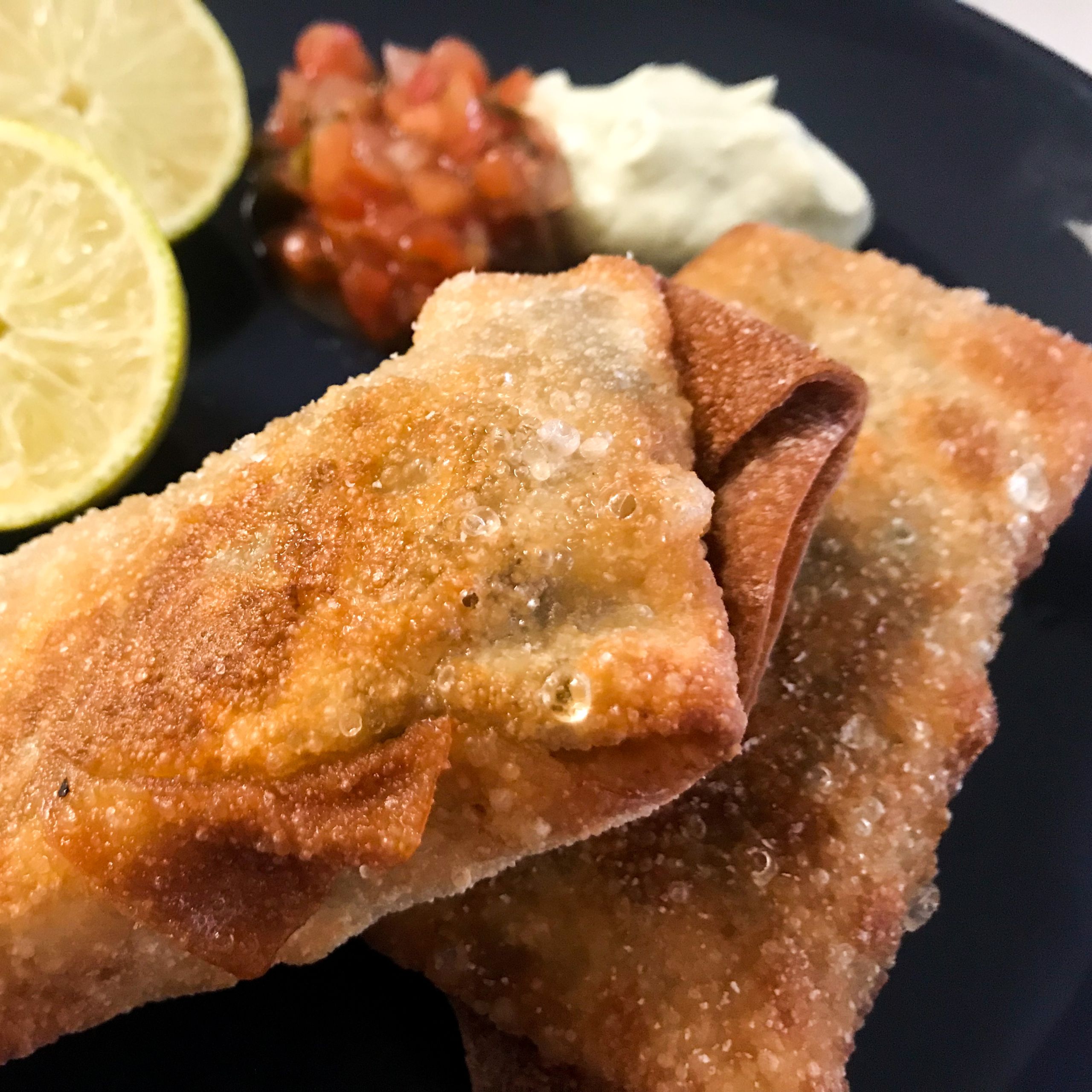 fried southwest egg rolls on plate with lime, salsa and crema | my curated tastes