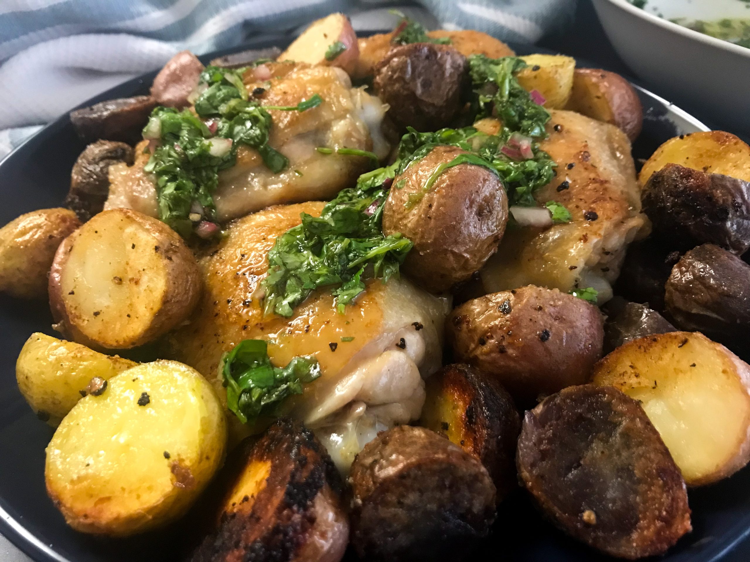 cooked chicken thighs and potatoes on a plate topped with chimichurri sauce | My Curated Tastes