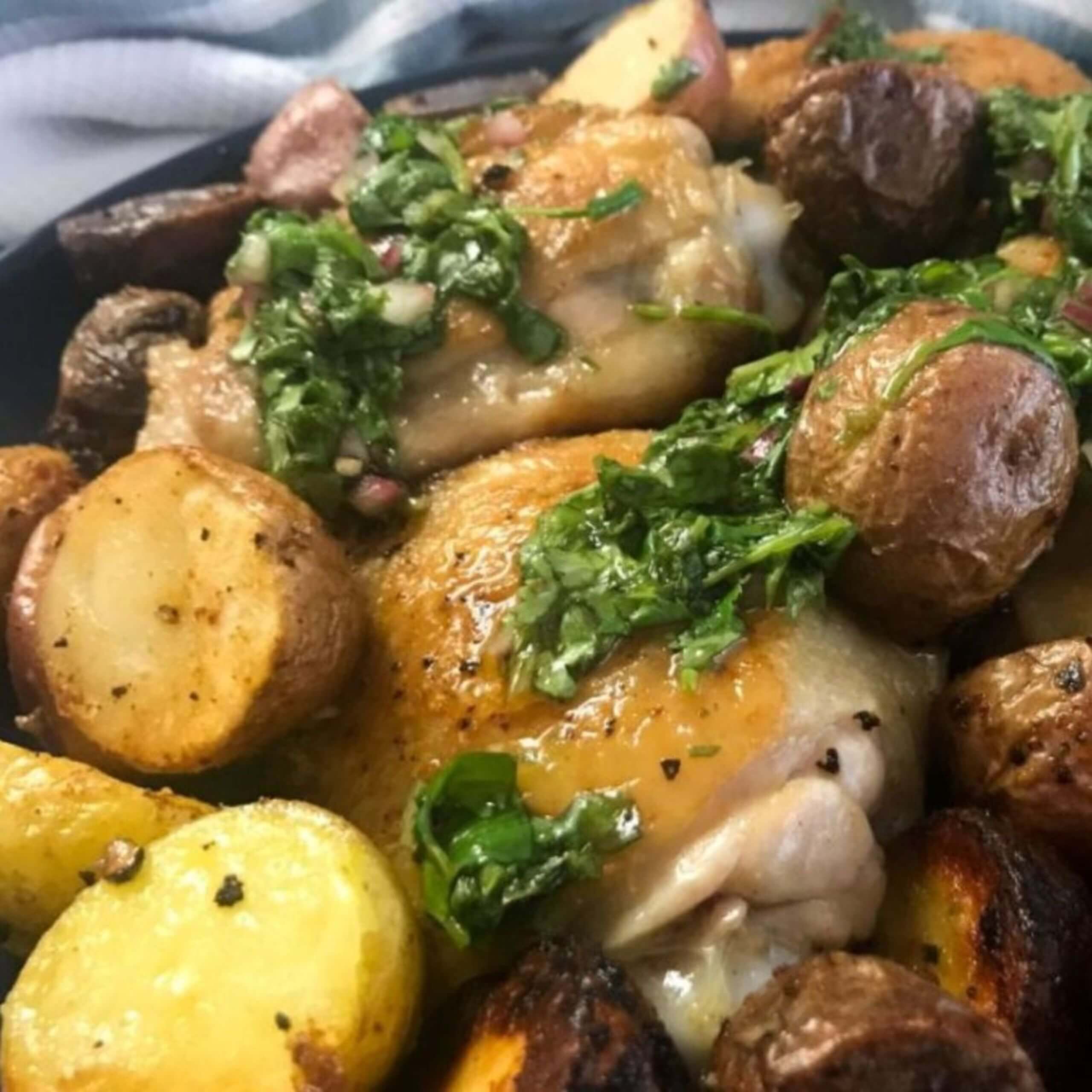 cooked chicken thighs and potatoes on a plate topped with chimichurri sauce | My Curated Tastes