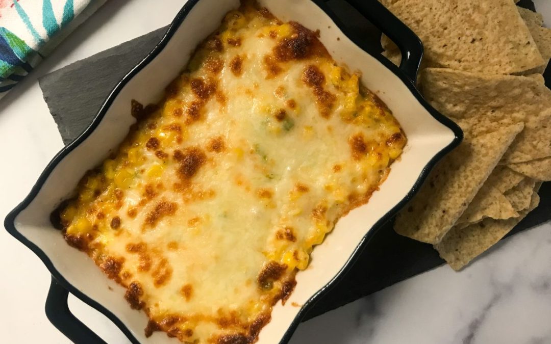 cheesy corn dip in a casserole dish with tortilla chips on the side