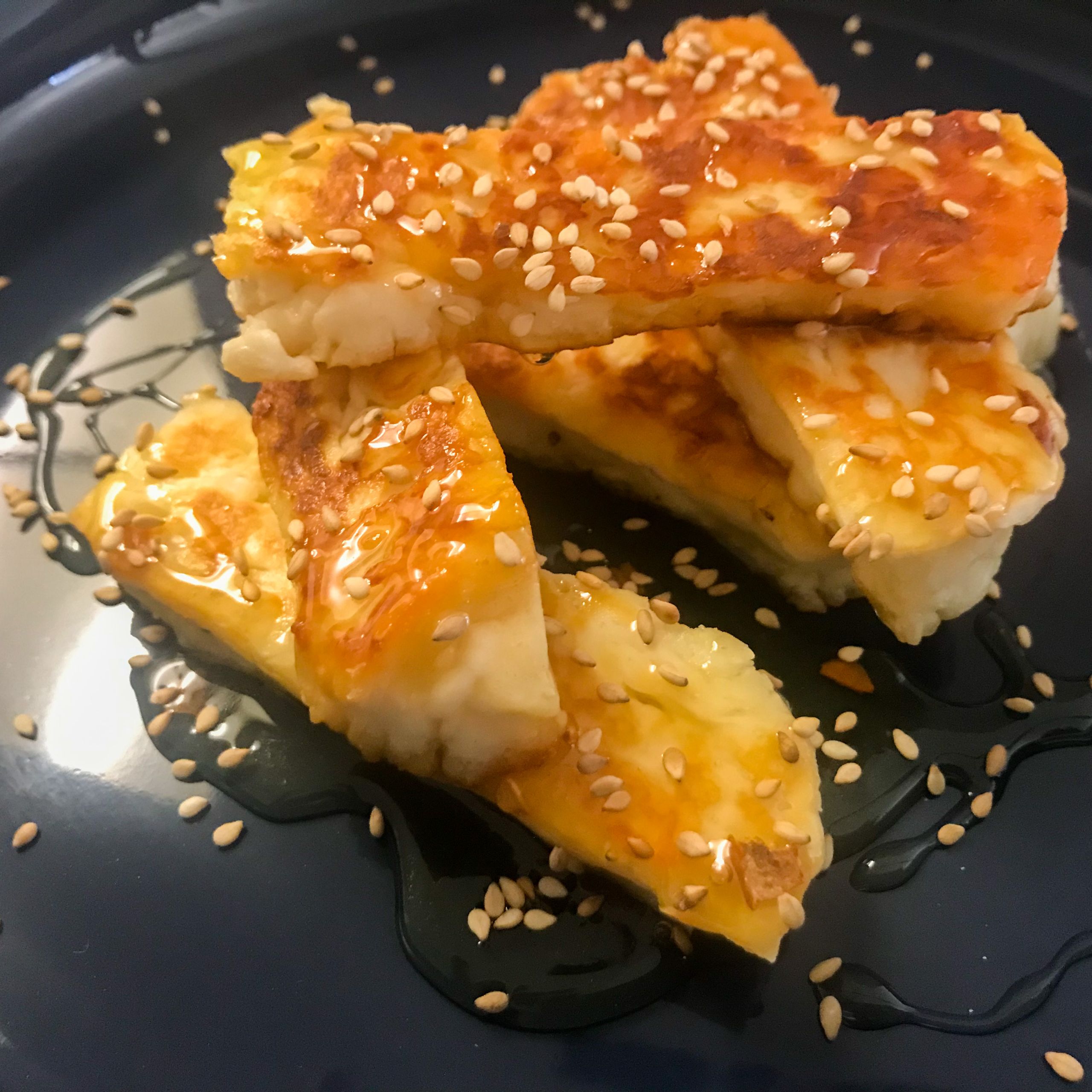 cooked halloumi fries on a platter with honey, chili flakes and sesame seeds