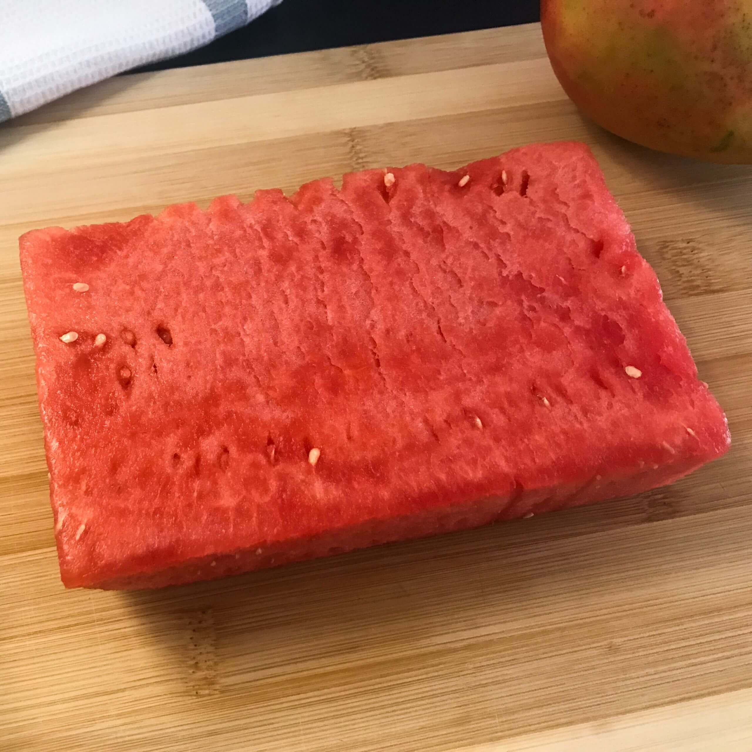chunk of watermelon and a mango on a cutting board