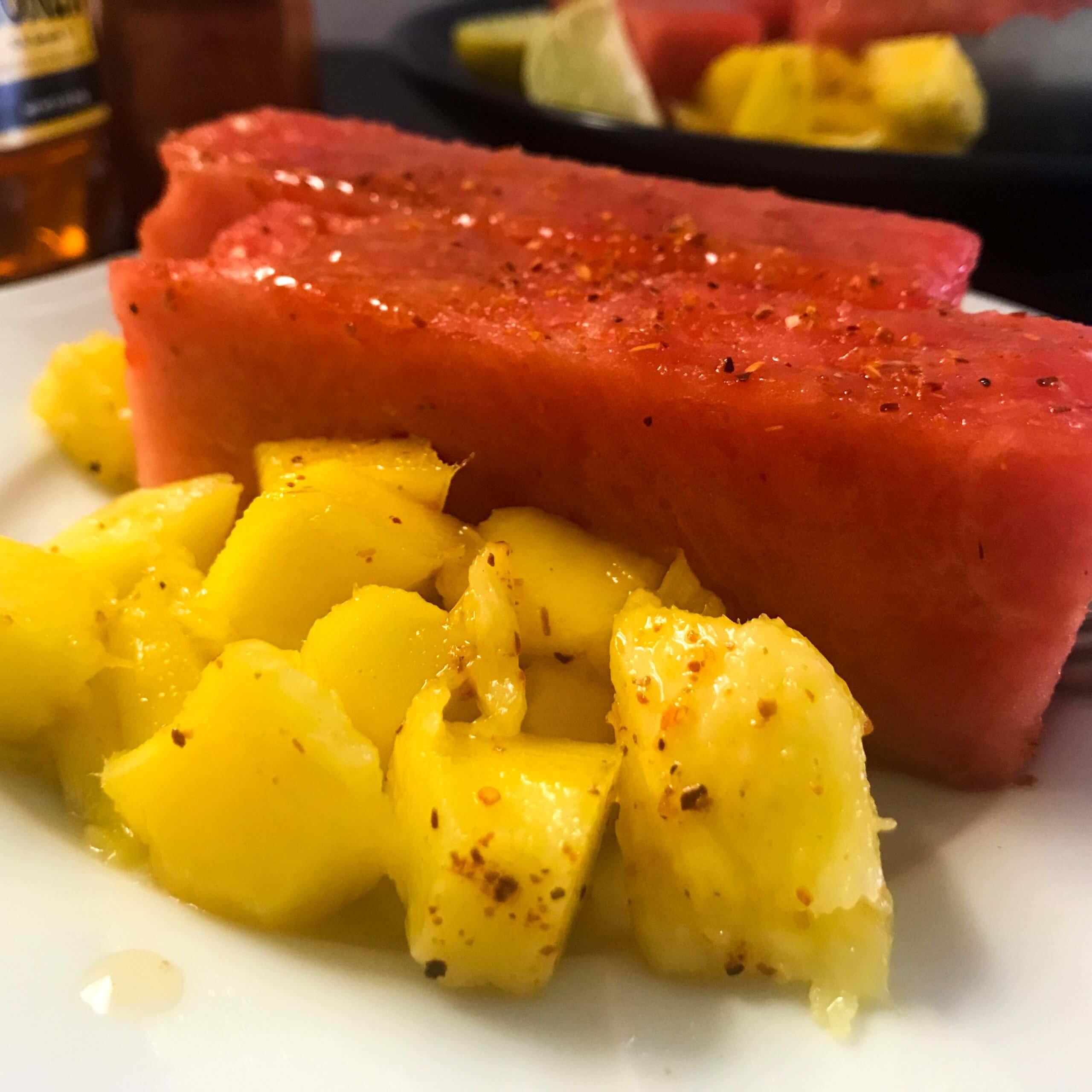 cut watermelon and chopped mango with tajin seasoning and honey on a plate