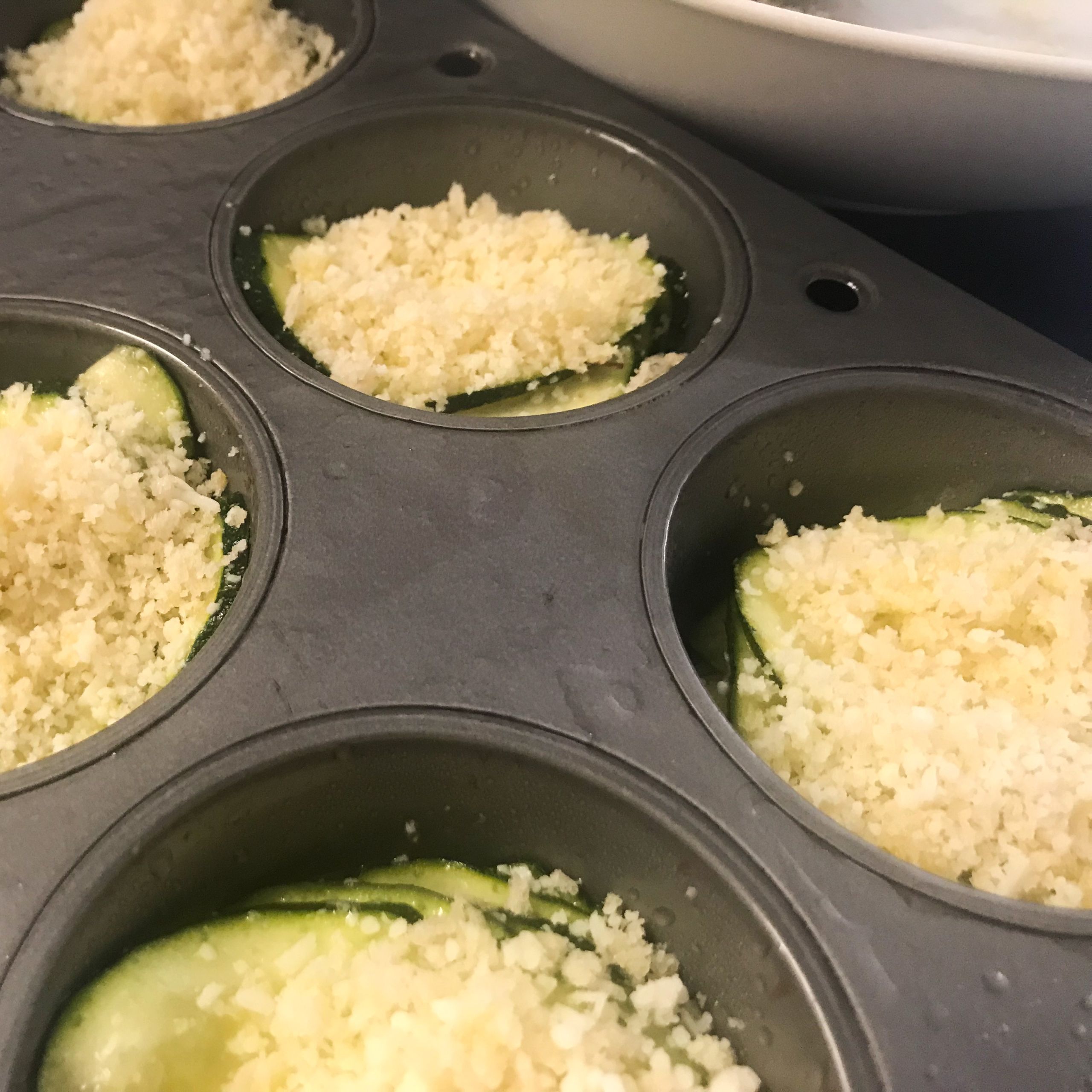 sliced zucchini in muffin tins topped with cheese and panko