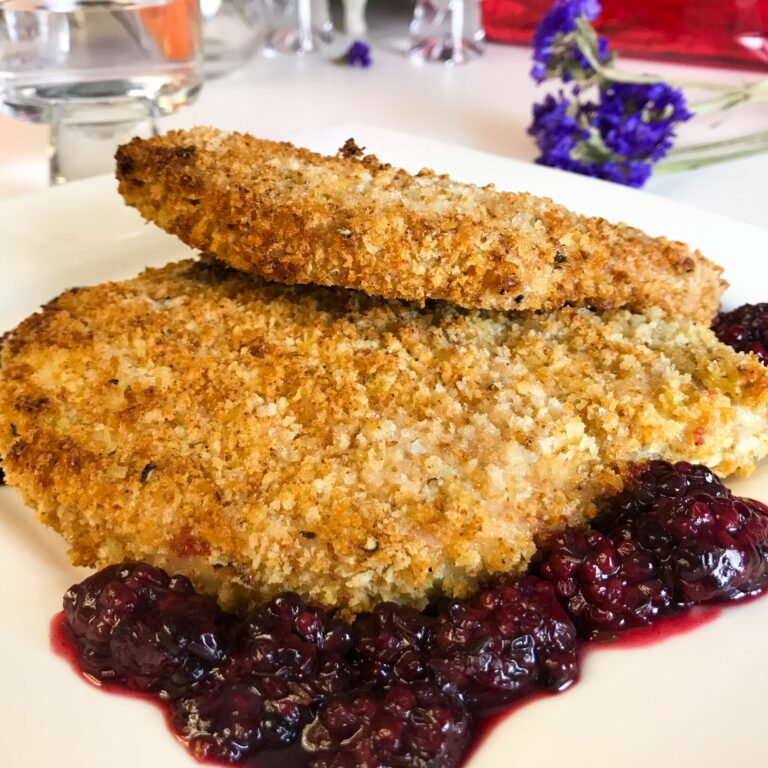 breaded baked pork chops on a platter with blackberry sauce.