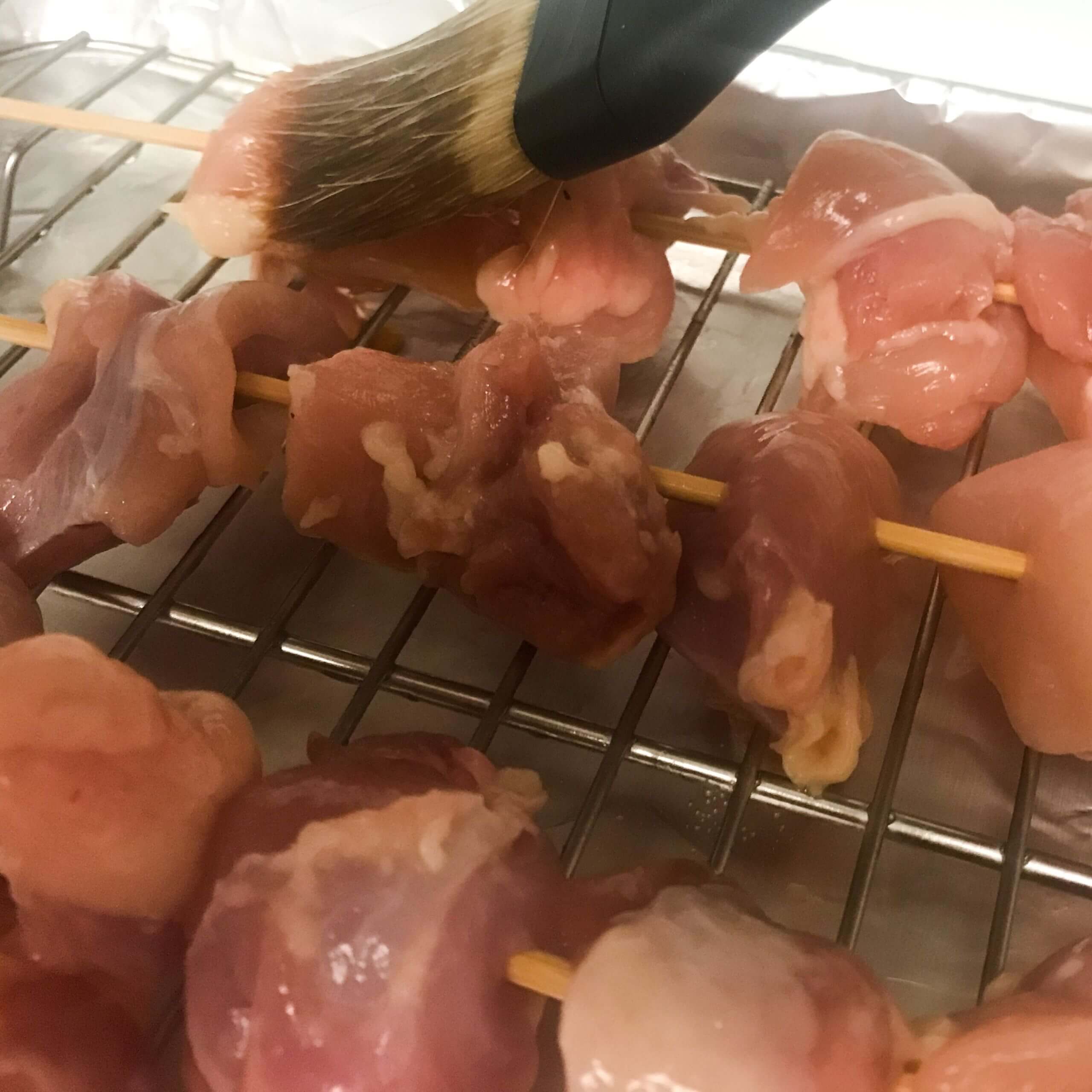 raw chicken on skewers being basted