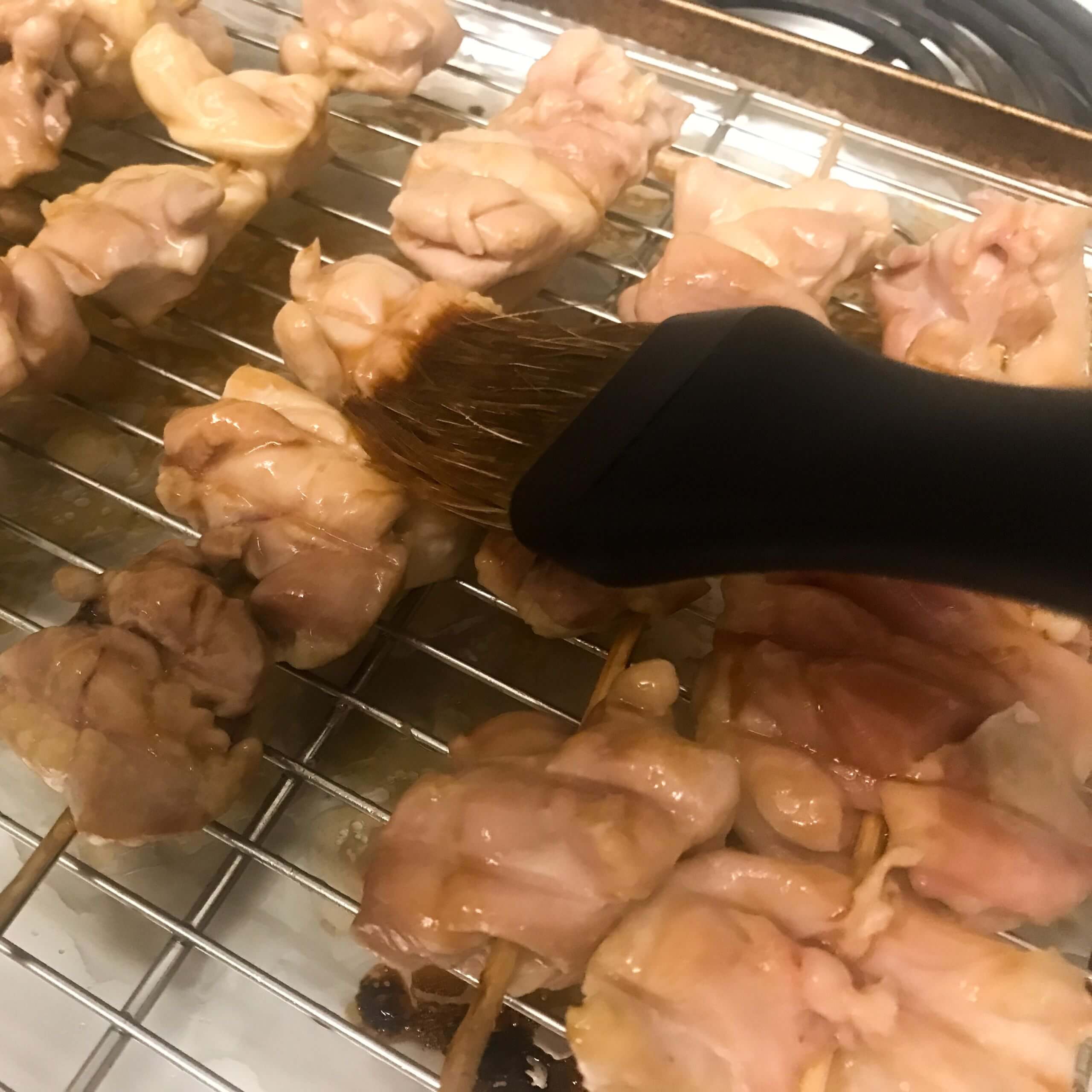 chicken skewers being basted with sauce