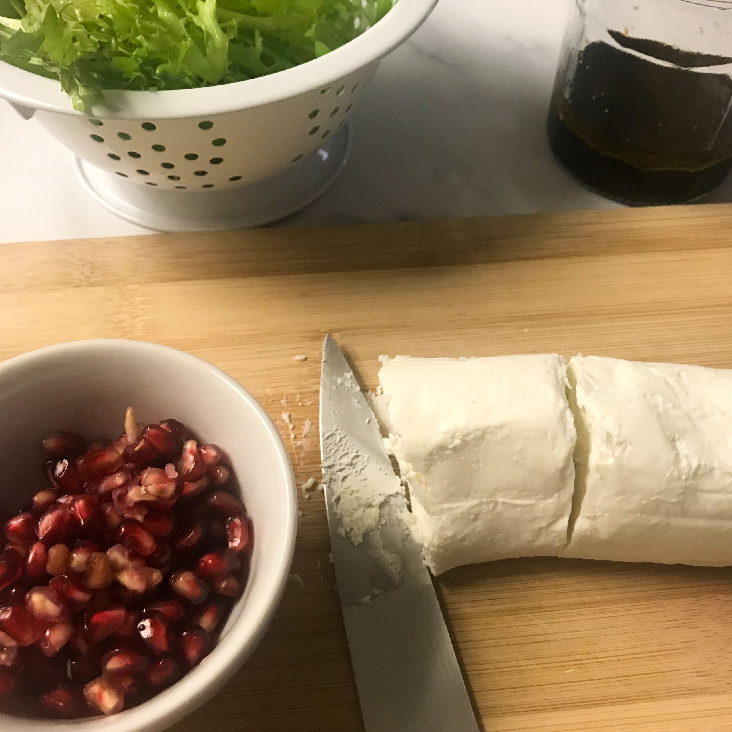 lettuce, pomegranate seeds, dressing and goat cheese on counter