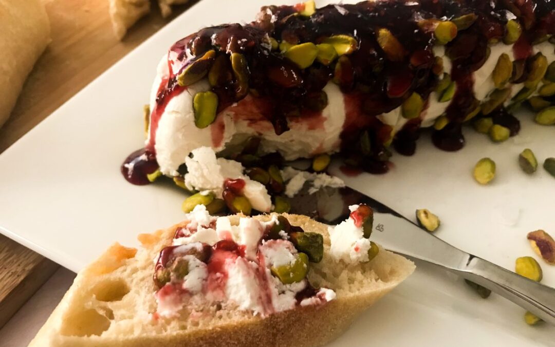 log of goat cheese covered in pistachios and raspberry preserves with a knife and bread