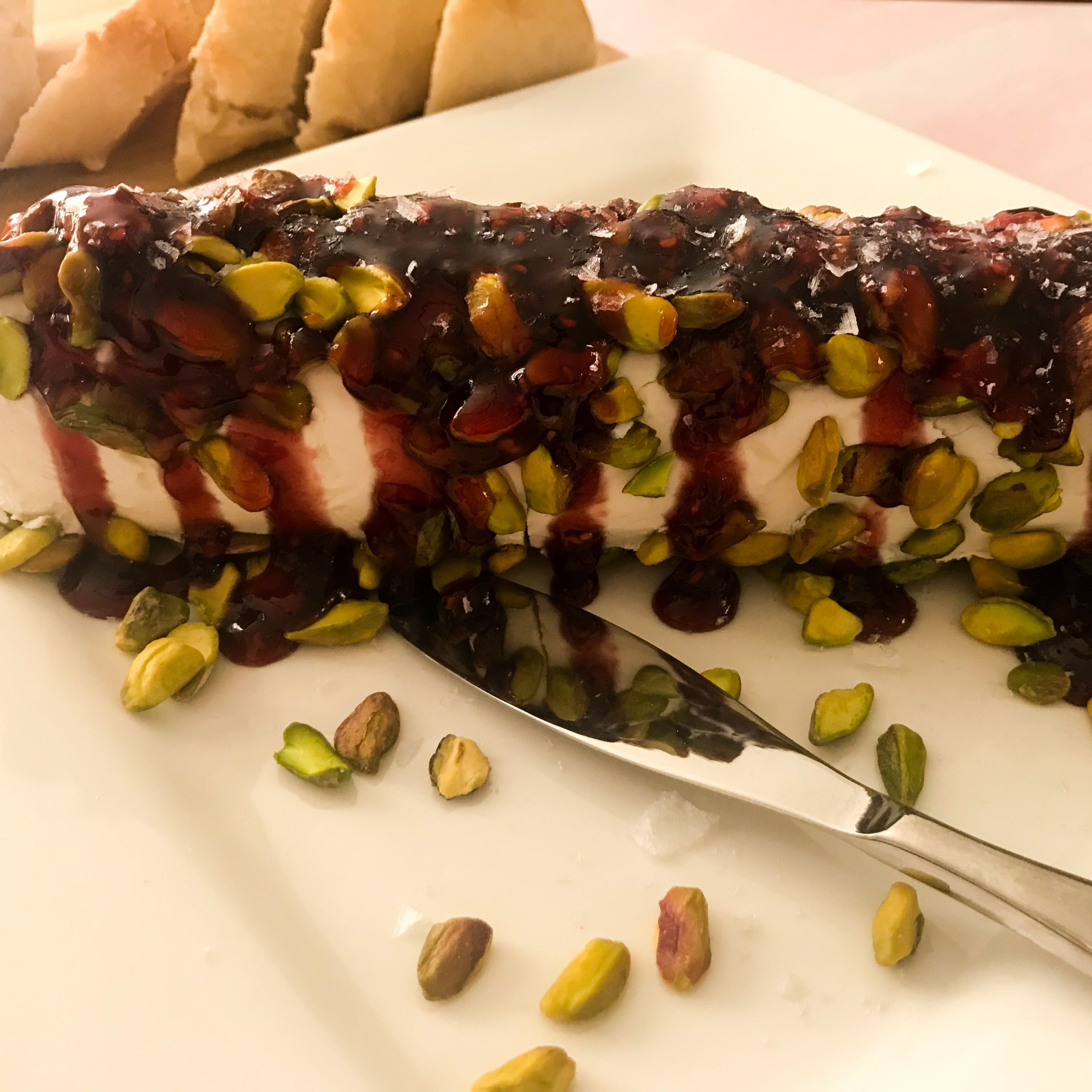 log of goat cheese covered in pistachios and raspberry preserves on a plate