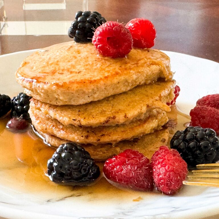 STACK OF OATMEAL FLOUR PANCAKES WITH BERRIES AND SYRUP.
