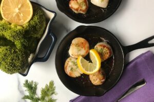 two cast iron skillets with scallops and lemon.