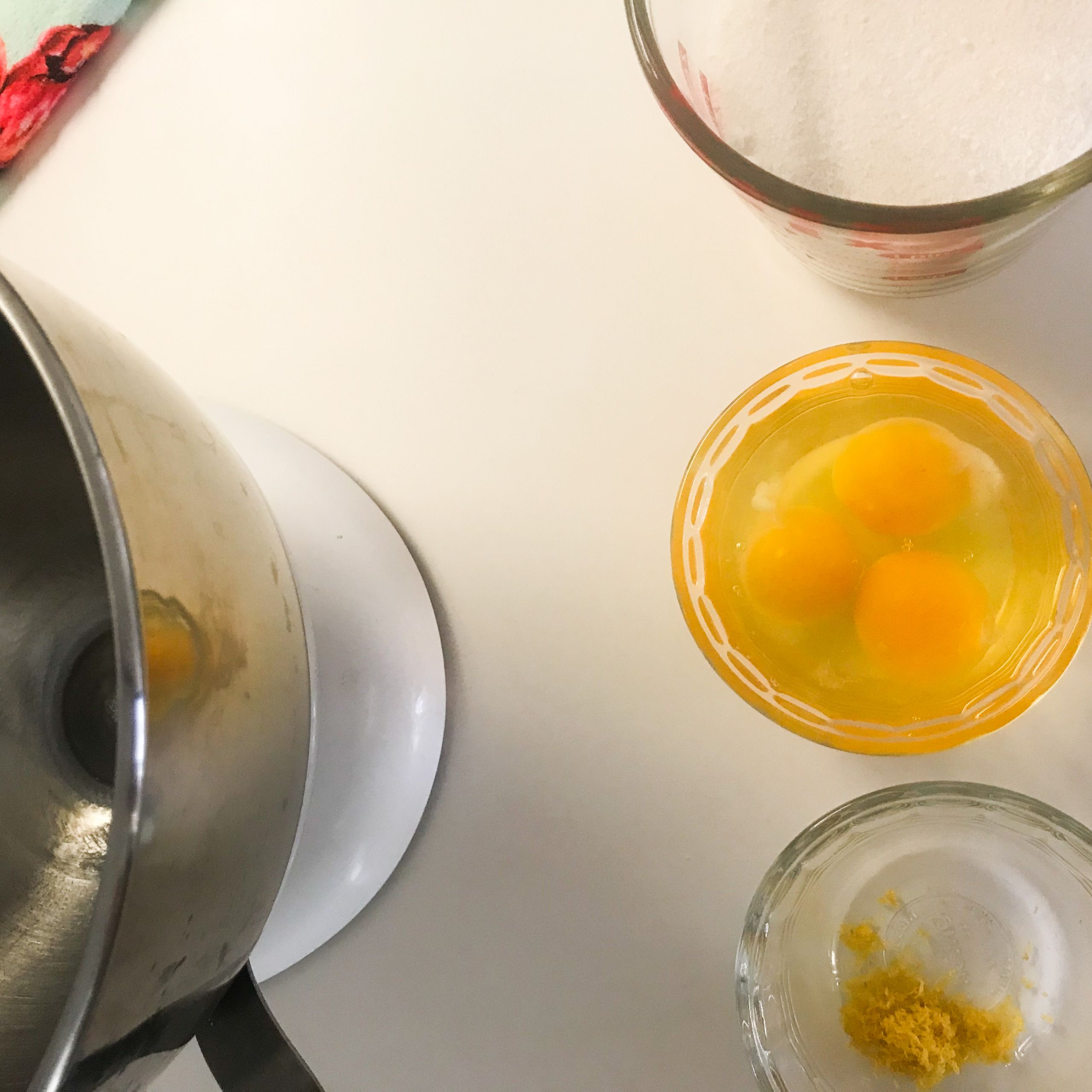 an empty mixing bowl, eggs in a bowl, sugar in a cup and lemon zest in a bowl