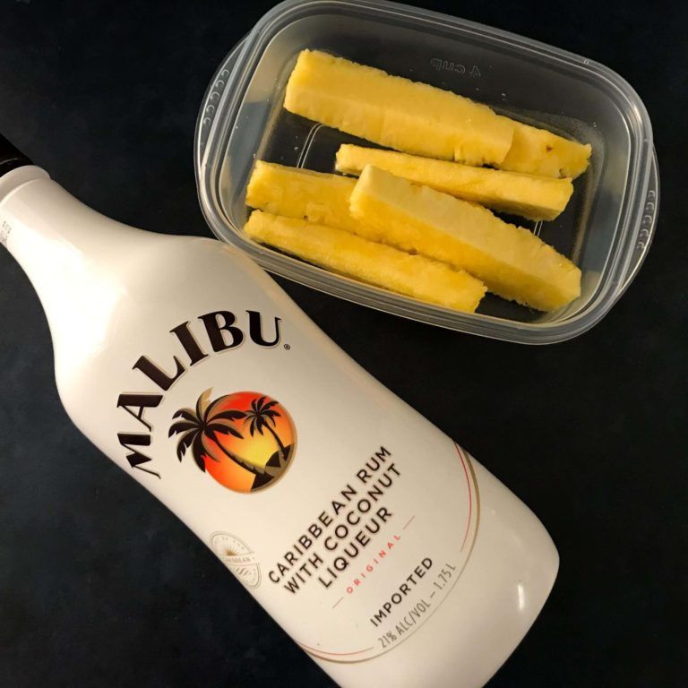 pineapple spears in container with bottle of rum.