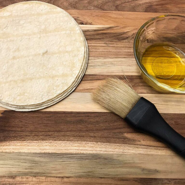 stack of tortillas next to bowl of olive oil and brush