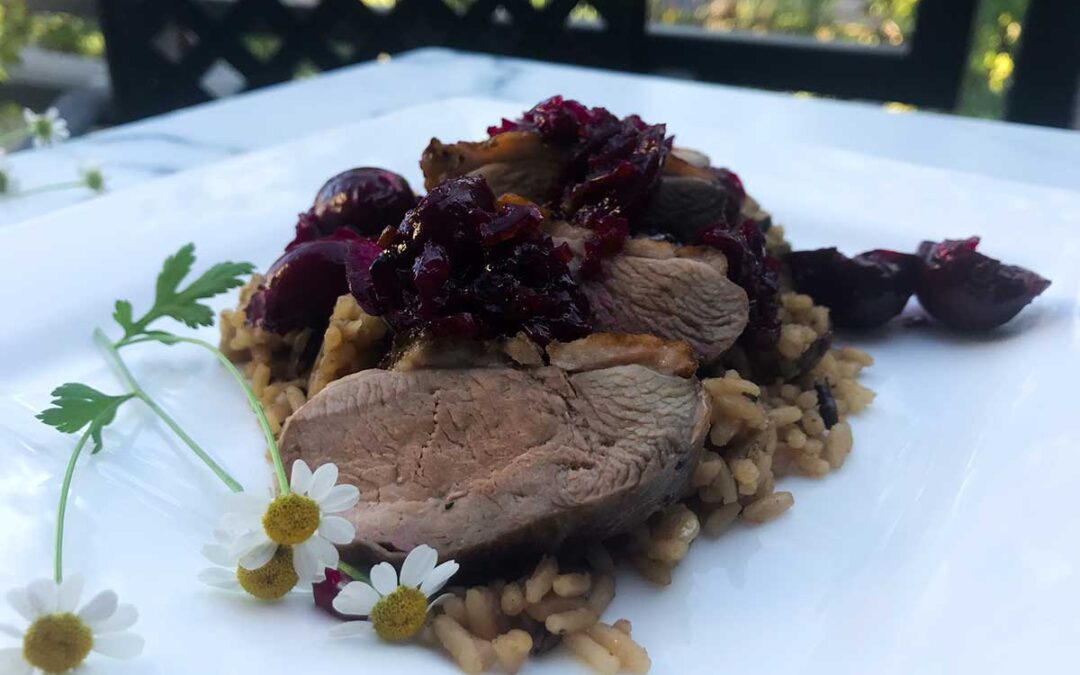 sliced duck breast over brown rice topped with cherry sauce on a plate