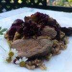 sliced duck breast over brown rice topped with cherry sauce on a plate