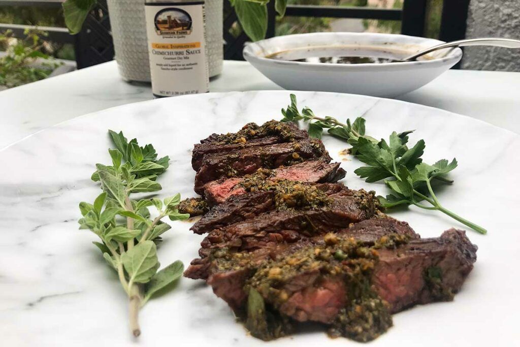 sliced skirt steak on a plate with chimichurri sauce and a bowl of sauce in the background