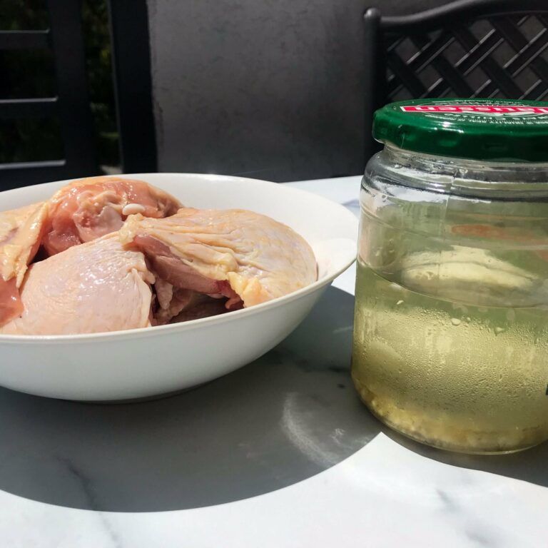 raw chicken in a bowl next to jar of pickle juice