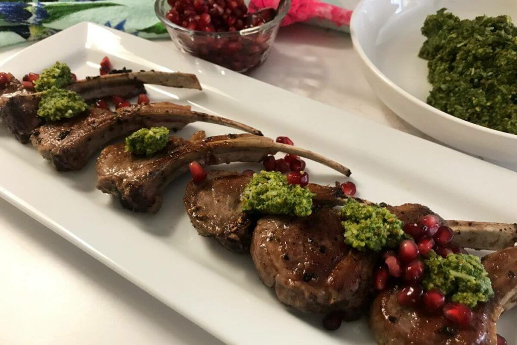 Platter of cooked lamb chops topped with pesto and pomegranate seeds.