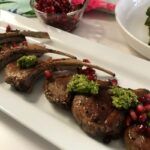 Platter of cooked lamb chops topped with pesto and pomegranate seeds.