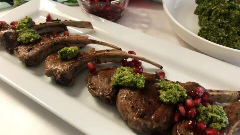 Platter of cooked lamb chops topped with pesto and pomegranate seeds.