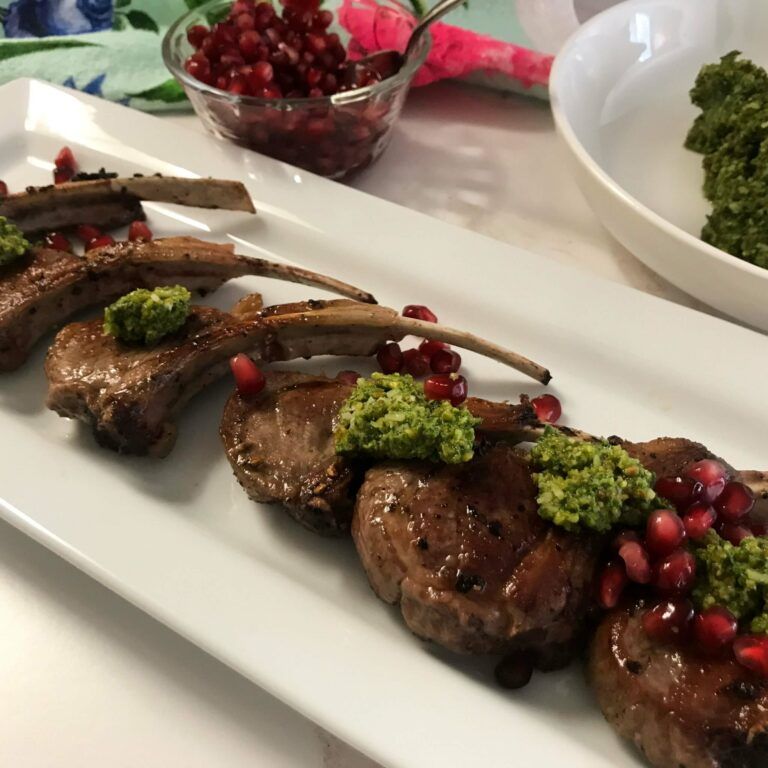 plated and cooked lamb chops topped with pesto and pomegranate seeds