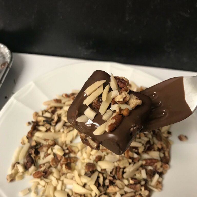 a fork holding a dipped banana bite with nuts.