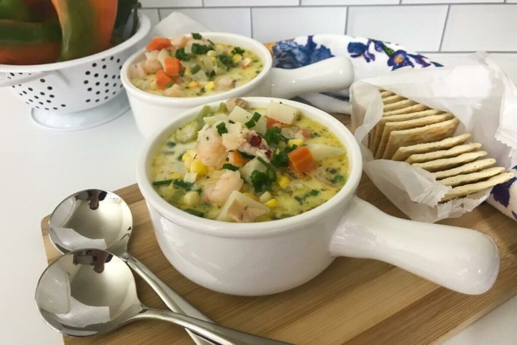 two bowls of shrimp and lobster soup with spoons and crackers on a board