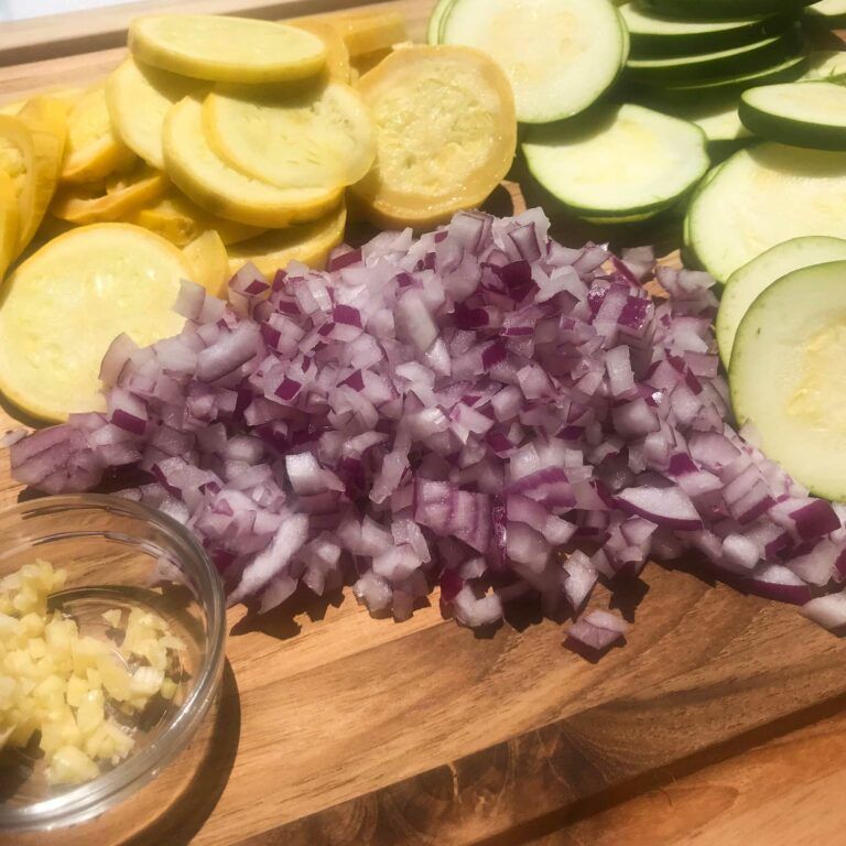 chopped onion with sliced squash on a board