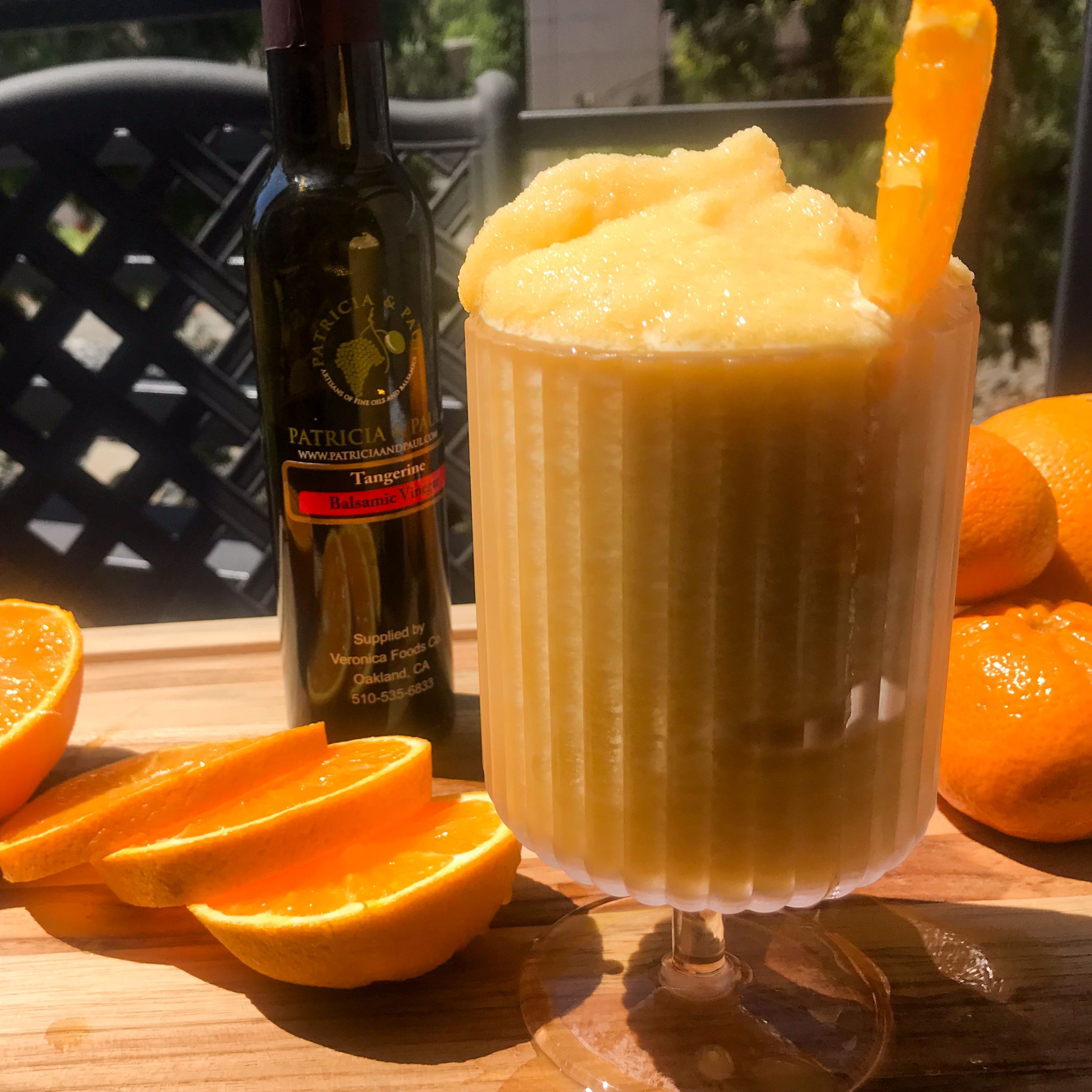 A glass of frozen orange aperol spritze with bottle of vinegar and sliced oranges