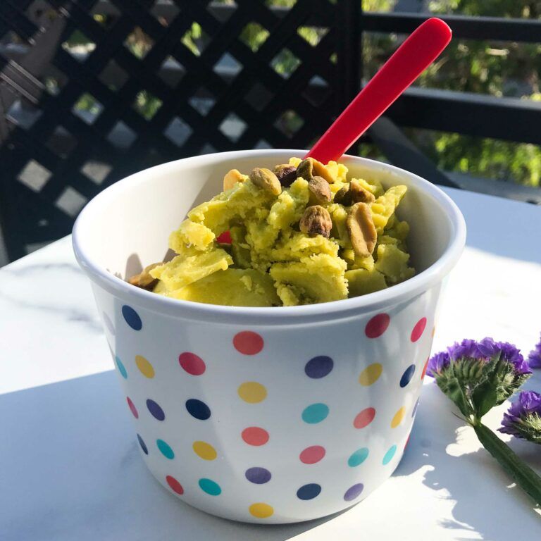cup of pistachio ice cream with spoon and nuts on top