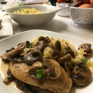 plated chicken marsala with bowl of noodles in background