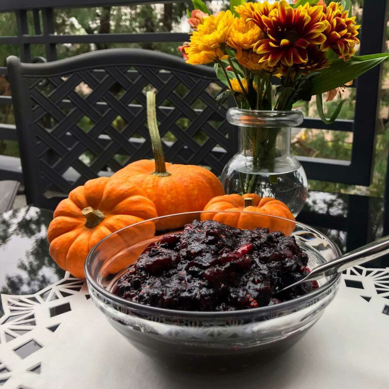 bowl of cranberry and elderberry sauce next to flowers and mini pumpkins
