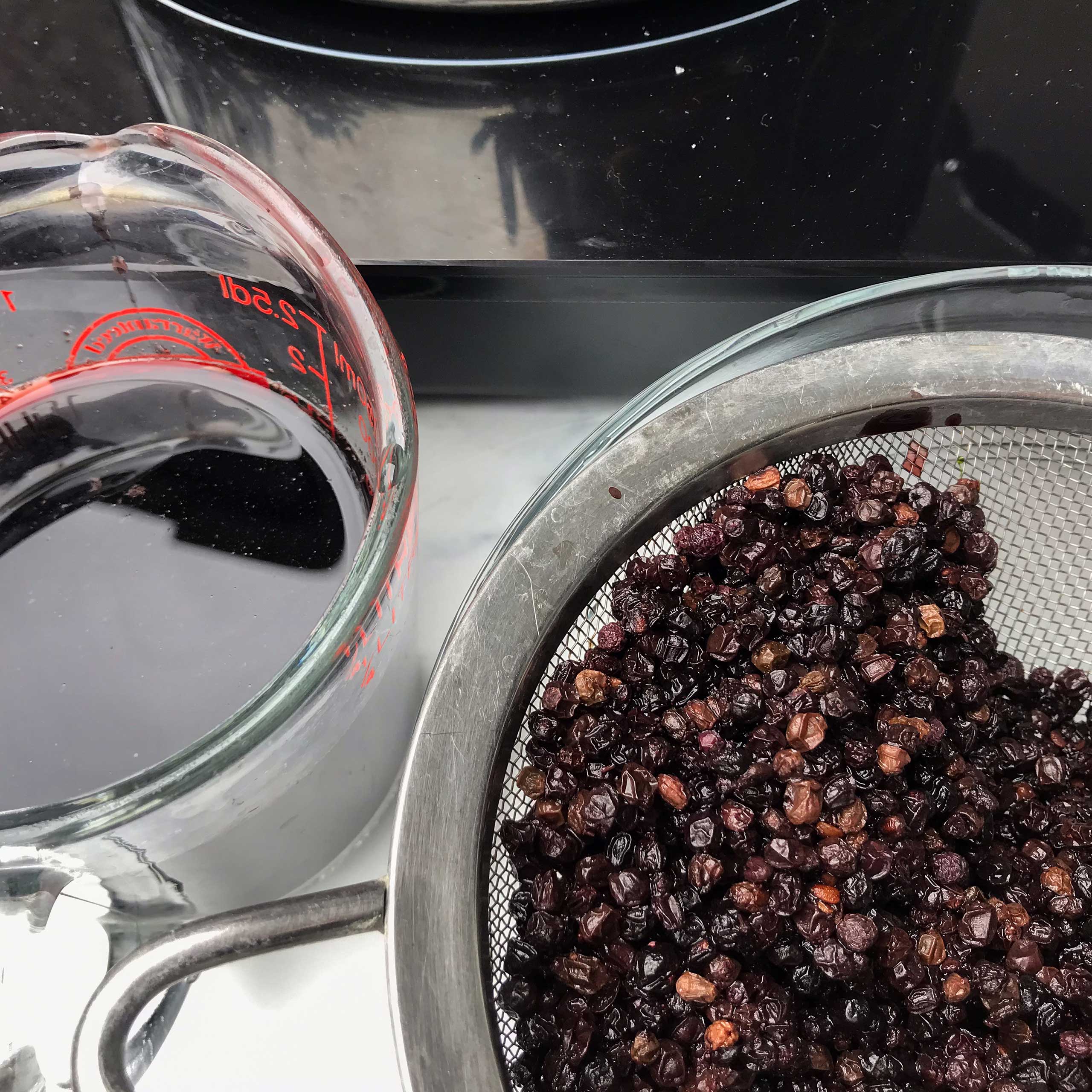 elderberries drained in sifter next to glass of elderberry soaking water