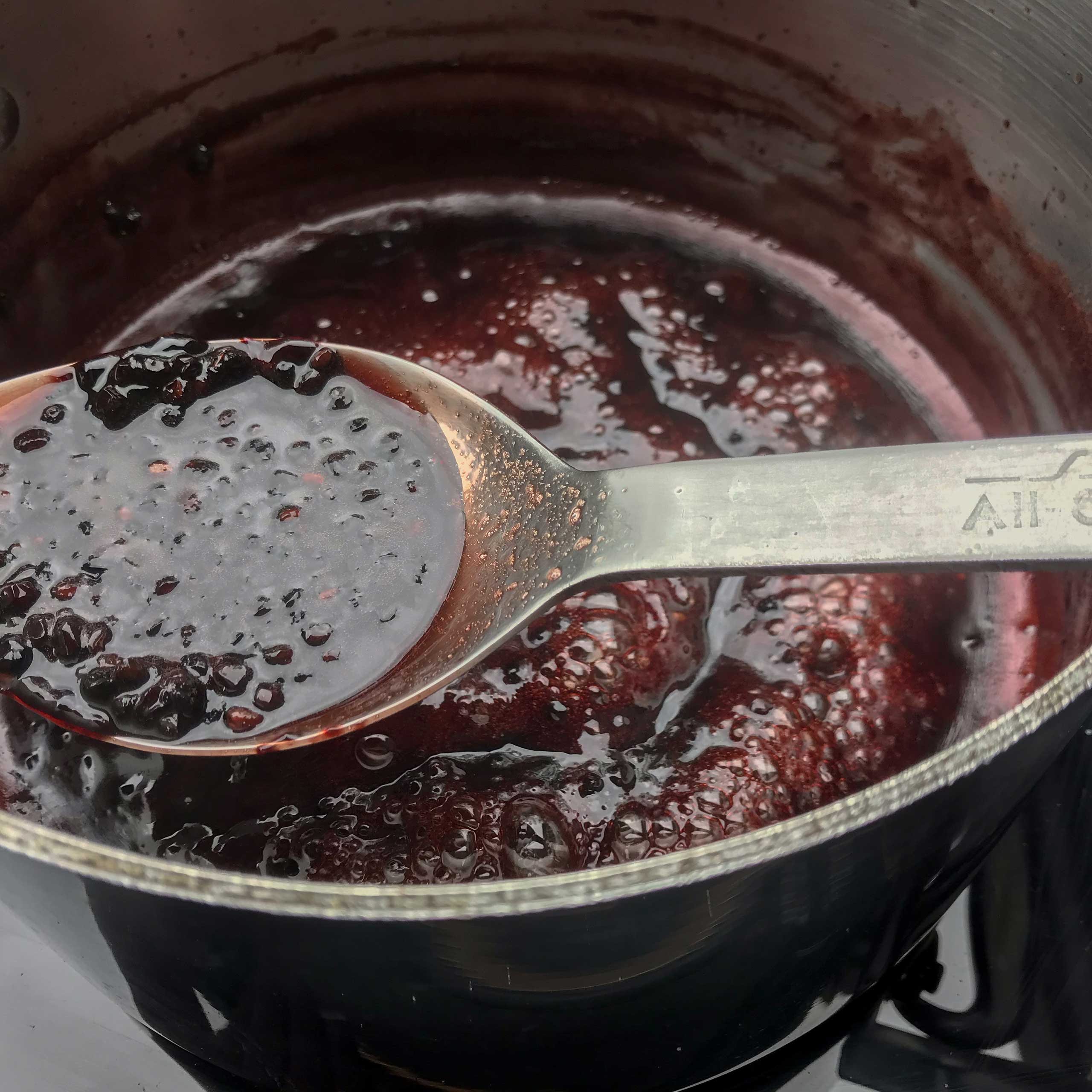a spoon of the thickened jam and the pot on stove