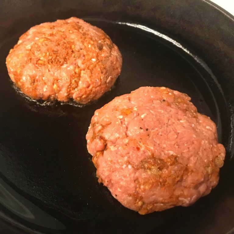 two raw burger patties cooking in skillet