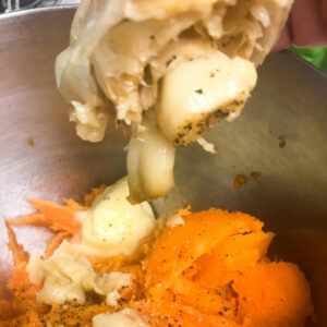 squeezing out cooked garlic cloves into bowl with sweet potatoes